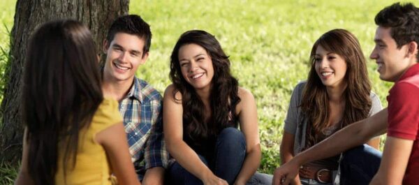 Teens sitting in a semicircle under a tree.