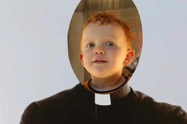 Boy looking through a priest cutout.