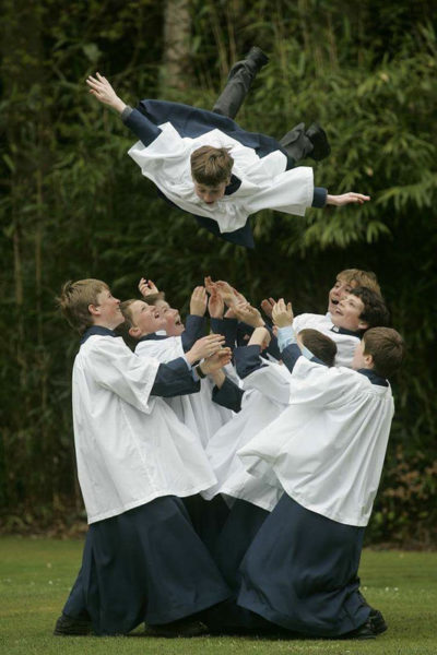 young boys dressed as altar servers tossing a boy into the air.