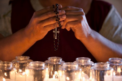 Woman's hands praying over candles with rosary.